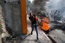 A woman runs past burning tyres as people protest against Haiti’s Prime Minister Ariel Henry earlier in February (Odelyn Joseph/AP)