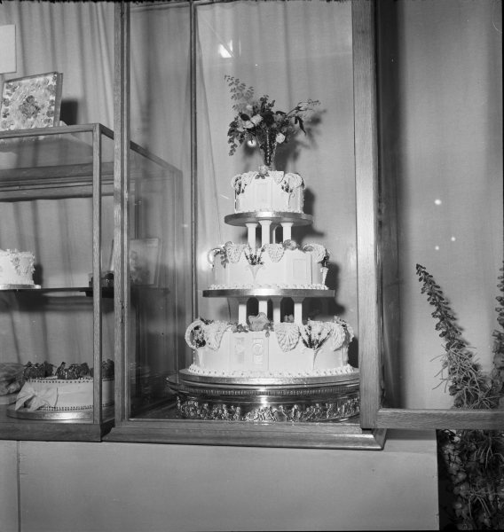 A three-tier iced cake on display in a glass case 